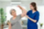 Physiotherapist helping an elderly woman with shoulder movement exercises during a home physiotherapy visit in London