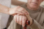 Caregiver holding elderly man's hands while supporting person living with Parkinson's disease